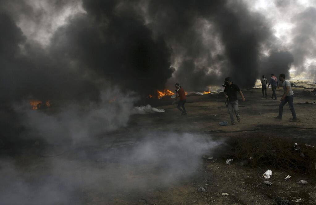 Palestinian protesters try to throw back teargas canisters fired by Israeli troops between the smoke of burned tires, during a protest at the Gaza Strip's border with Israel, east of Khan Younis, Friday, May 4, 2018. Huge clouds of black smoke from burning tires mixed with streaks of Israeli tear gas volleys Friday, as several thousand Palestinians staged their sixth weekly protest on the sealed Gaza-Israel border. At least 70 Palestinians were wounded by Israeli fire, the lowest casualty toll since protests began. (AP Photo/Adel Hana)