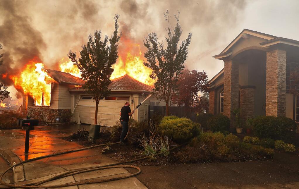 Chris Neace puts water on a structure fire in an attempt to keep the fire from spreading to another home in the Fountaingrove area of Santa Rosa on Monday, October 9, 2017. (Christopher Chung/ The Press Democrat)