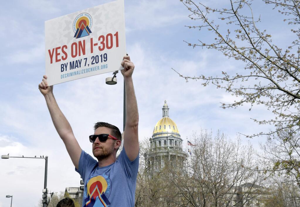 Chris Olson holds a sign near a busy intersection in downtown Denver on Monday, May 6, 2019, as he urges voters to decriminalize the use of psilocybin, the psychedelic substance in 'magic mushrooms.' Voters will decide Tuesday whether Denver will become the first U.S. city to decriminalize the drug. (AP Photo/Thomas Peipert)