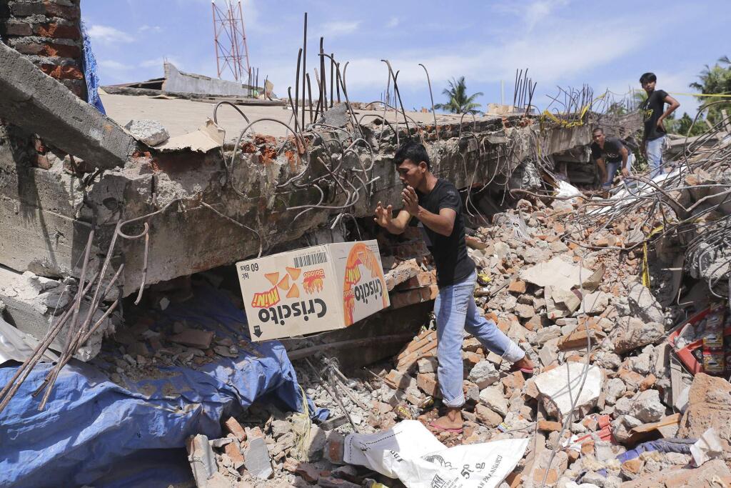 A man removes a box of food from under the rubble of a building that collapsed after an earthquake in Pidie Jaya, Aceh province, Indonesia, Wednesday, Dec. 7, 2016. A strong undersea earthquake rocked Indonesia's Aceh province early on Wednesday, killing a number of people and causing dozens of buildings to collapse. (AP Photo/Heri Juanda)