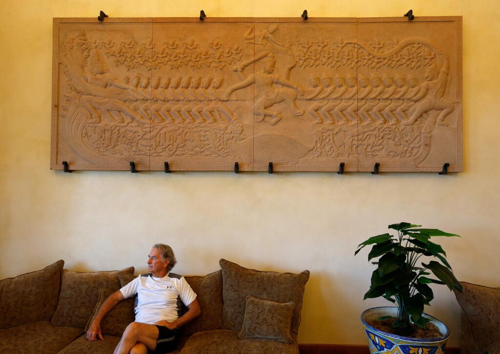 George Googins sits in his great room beneath the one-ton stone carving that he commissioned to depict a temple carving from Angkor Wat, at his home in Petaluma, California, on Friday, July 14, 2017. (Alvin Jornada / The Press Democrat)
