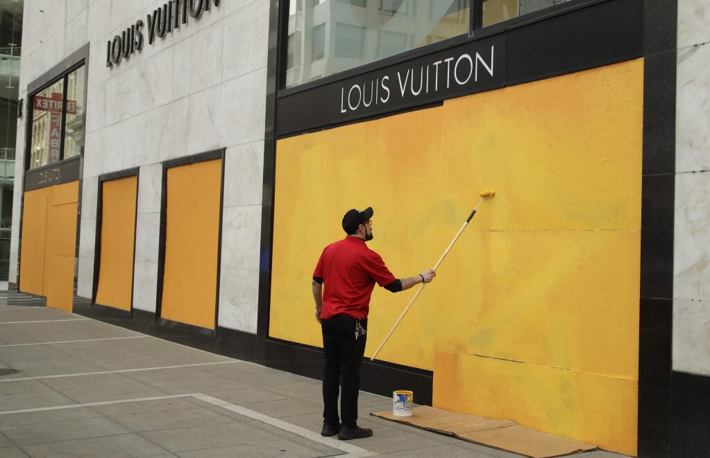 A worker paints over a Louis Vuitton storefront boarded up due to the coronavirus outbreak on Monday, March 30, 2020, in San Francisco. (AP Photo/Ben Margot)
