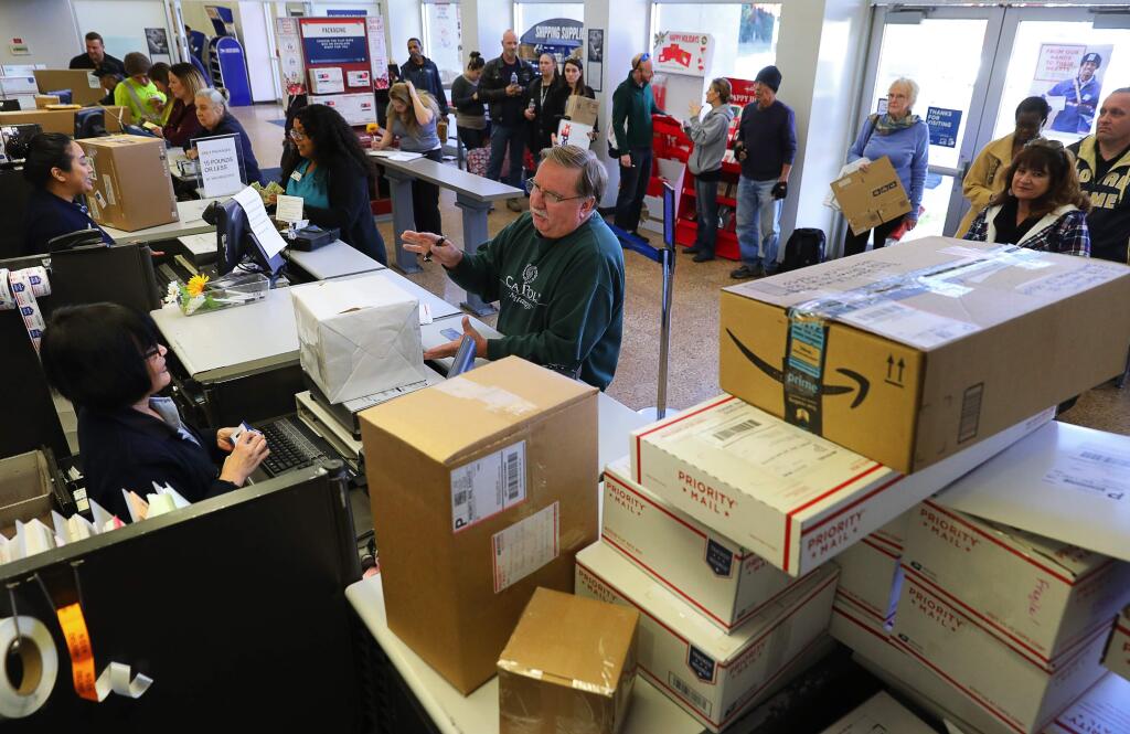 U.S. Postal Service sales service associate Guoping Liu, left, helps Mark Hilburn send a package in time for Christmas at the downtown in Santa Rosa Post Office on Monday, December 18, 2017. (Christopher Chung/ The Press Democrat)