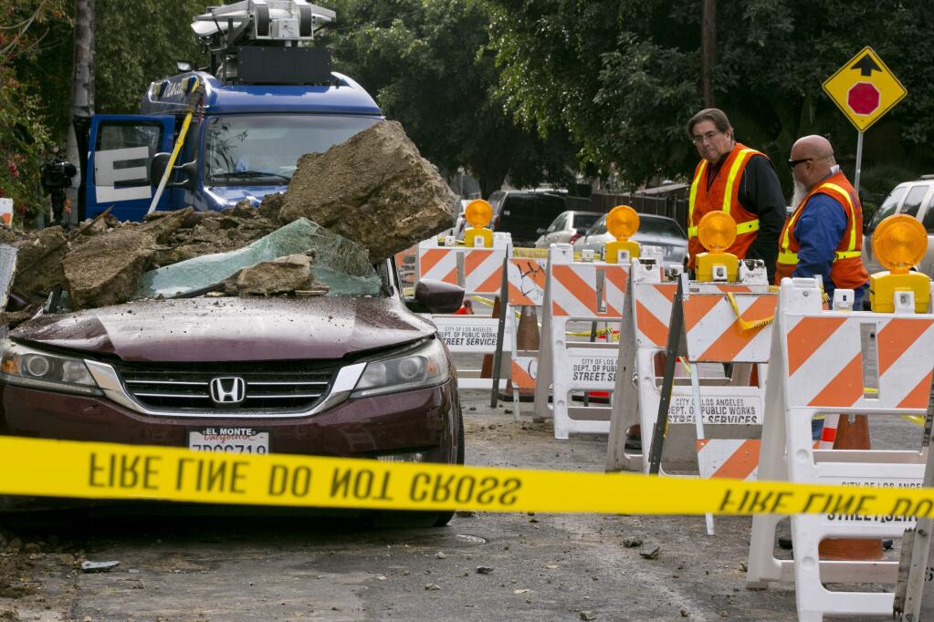 Southern California Gas Company, SoCalGas employees check residential broken gas lines, as a vehicle is buried under mud and concrete slabs as debris slid early morning from beneath a house in Los Angeles, Friday, Jan. 18, 2019. No one was hurt. The three-day drenching put a dent in California's drought. (AP Photo/Damian Dovarganes)