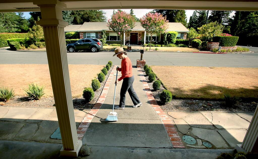 On Pear Tree Court in Sonoma, Jackie Lee sweeps the previous days leaves away. The entire street has brown lawns, Friday Aug. 7, 2015 in Sonoma. (Kent Porter / Press Democrat) 2015