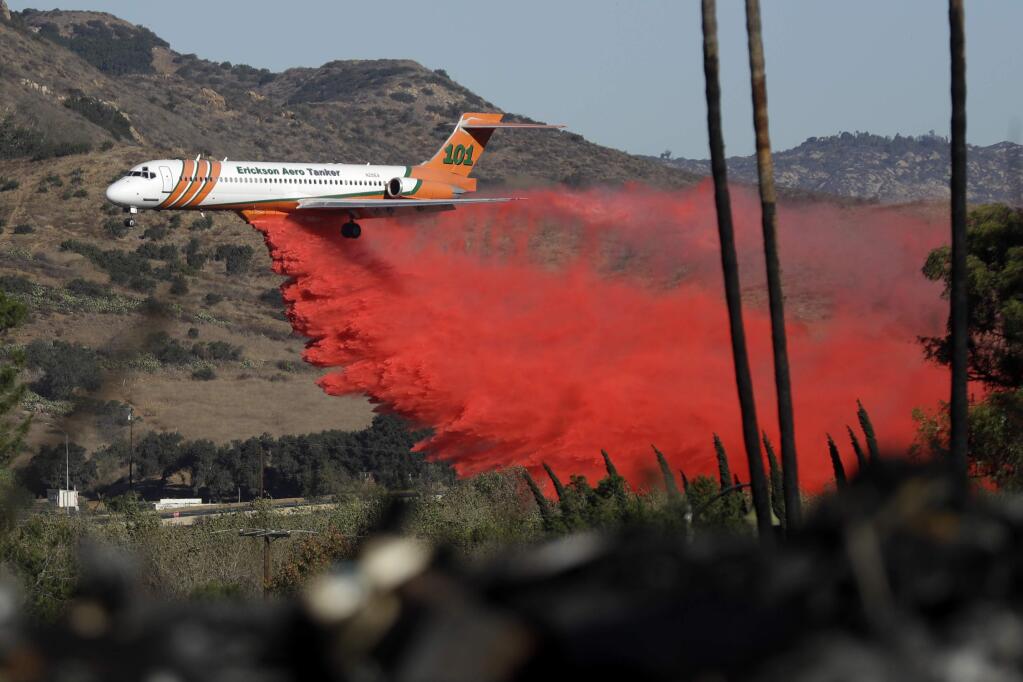 A plane drops fire retardant on a wildfire Friday, Dec. 8, 2017, in Fallbrook, Calif. The wind-swept blazes have forced tens of thousands of evacuations and destroyed dozens of homes in Southern California. (AP Photo/Gregory Bull)
