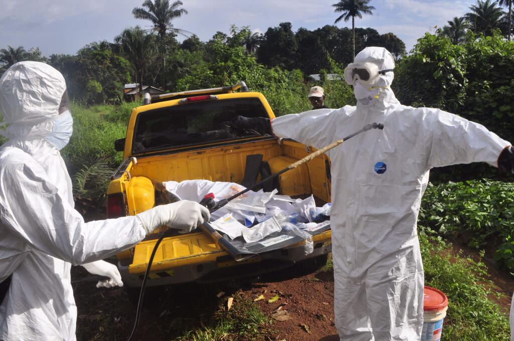 A health worker sprays disinfectant onto a colleague after they worked with the body of a man, suspected of contracting and dying form the Ebola virus on the outskirts of Monrovia, Liberia, Monday, Oct. 27, 2014. (AP Photo/Abbas Dulleh)