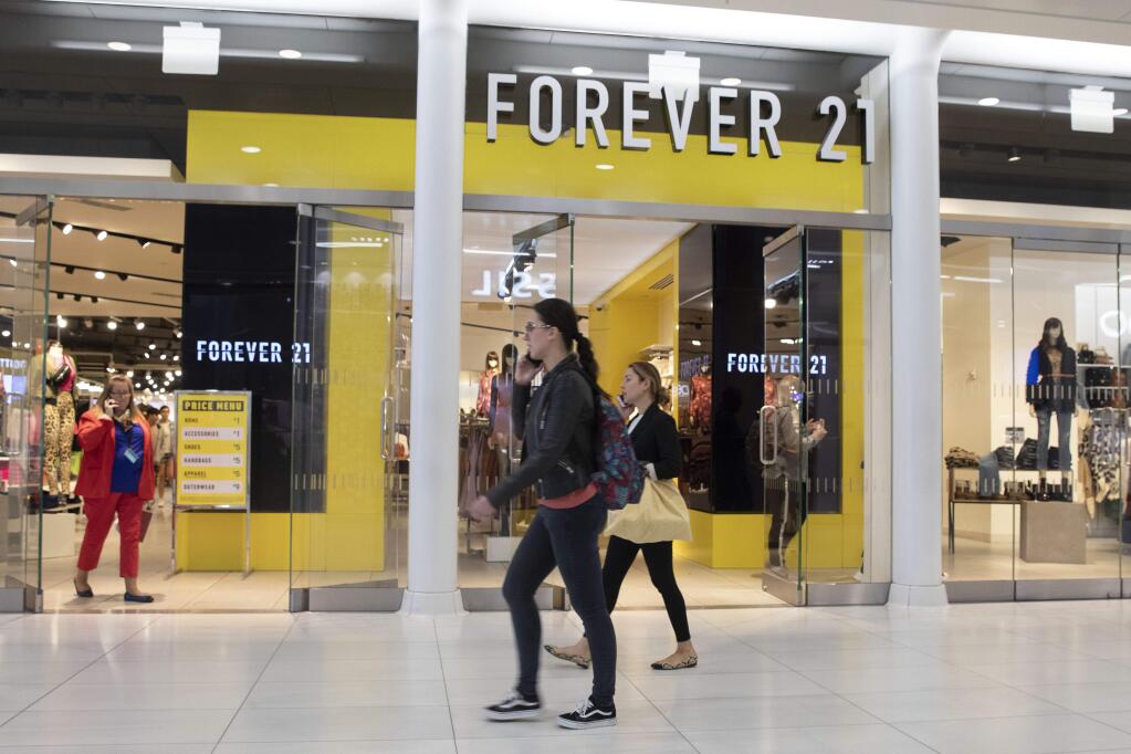 FILE - In a September 30, 2019 file photo, people walk in front of a Forever 21 clothing store in New York. A group that includes mall owners Simon Property Group, Brookfield Property Partners and brand business Authentic Brands Group are offering to buy trendy teen fashion retailer Forever 21 for approximately $81 million.(AP Photo/Mark Lennihan, File)