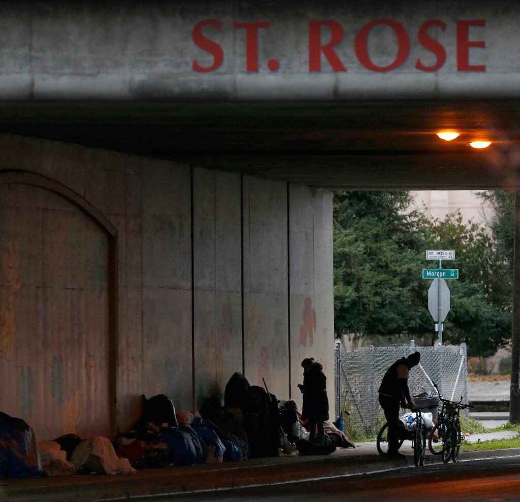 A group of homeless people with their belongings find shelter from the rain beneath a Highway 101 overpass in Santa Rosa in January 2017. (ALVIN JORNADA / The Press Democrat)