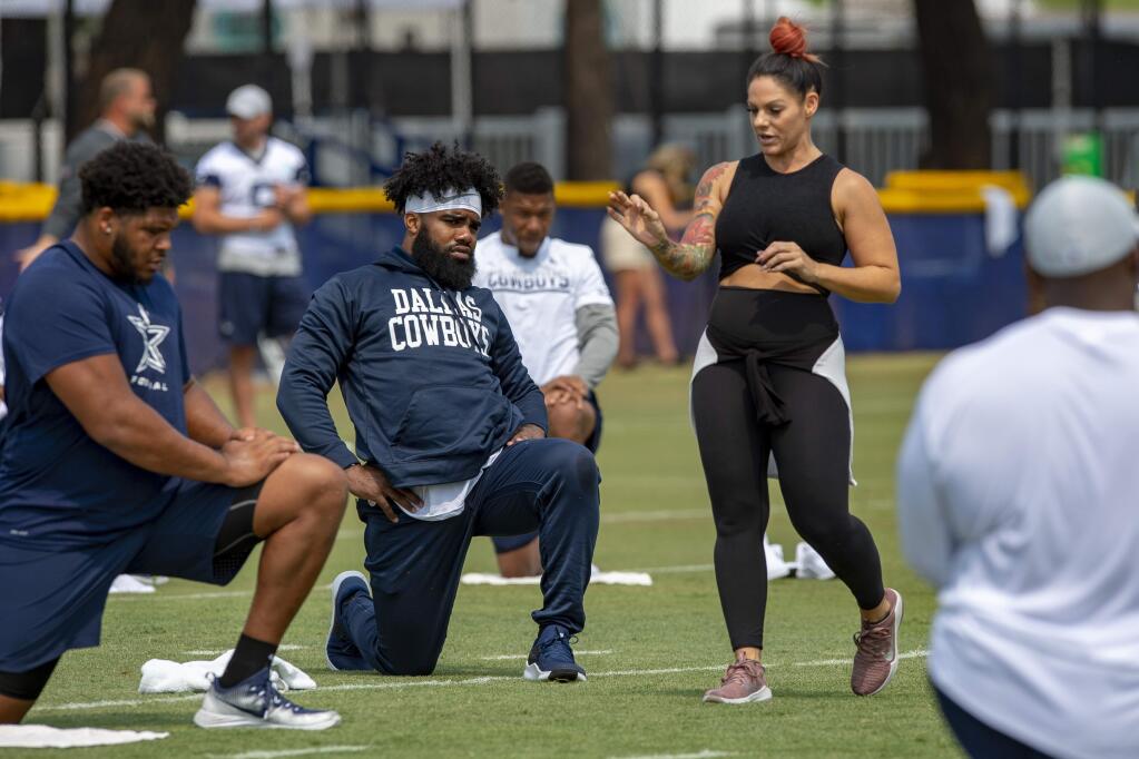In this July 28, 2018, file photo, Dallas Cowboys offensive tackle La'el Collins, left and running back Ezekiel Elliott, center, listen to yoga instructor Stacey Hickman, right, as the team does some flexibility exercises at training camp in Oxnard. (AP Photo/Gus Ruelas, File)