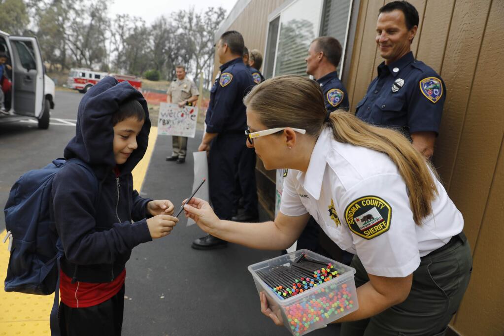 Karen Hancock, a community service officer with the Sonoma County Sheriff's Office hands a pencil to Victor Mazariego, 7, on the first day of class at the Redwood Adventist Academy campus after the Tubbs fire destroyed the school in October. Photo taken in Santa Rosa on Monday, August 20, 2018. (Beth Schlanker/ The Press Democrat)