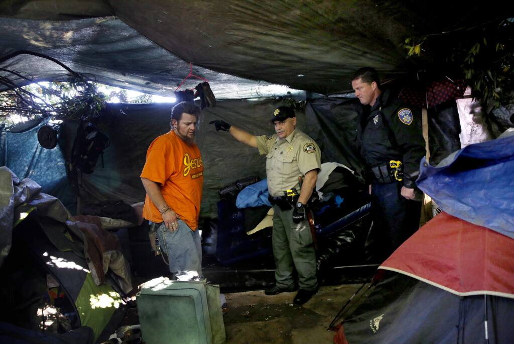 (From right) Santa Rosa police officer Jesse Cude and Sonoma County Sheriff's Deputy Jose Acevedo talk with Casey Easley in his tent as part of an effort by the Homeless Outreach Services Team at a homeless encampment on Mark West Creek near Almar Parkway in Santa Rosa, on Wednesday, April 8, 2015. (BETH SCHLANKER/ The Press Democrat) Sonoma Magazine