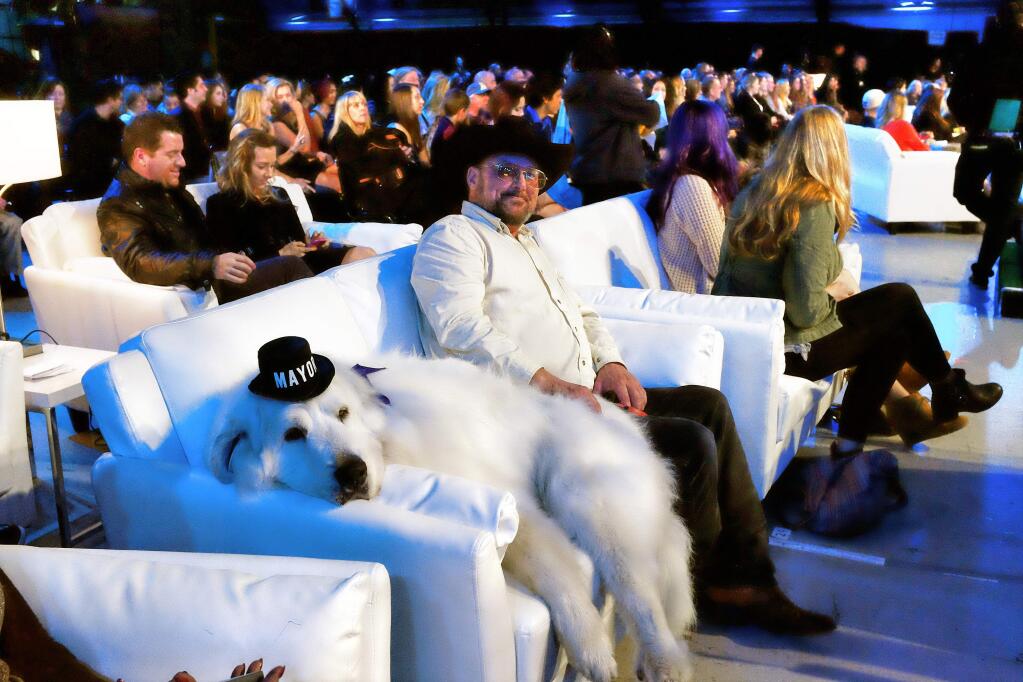 This Saturday, Jan. 10, 2015 photo Duke a 7 year old Great Pyrenees who was elected mayor In Cormorant, Minn. lounges on a couch with David Rick during the 2015 World Dog Awards at the Barker Hanger in Santa Monica. Awards season in Hollywood has begun. For at least one show, though, there will be no 'Lights, Camera, Action,' no tables to maneuver around, no long speeches and no seat fillers. That's because the show and nearly every award in it is going to the dogs. Canine winners, along with a few humans and a cat, will be presented with golden fire hydrant statuettes. Dogs will lounge on sofas and overstuffed chairs in front of the stage. (AP Photo/Richard Vogel)