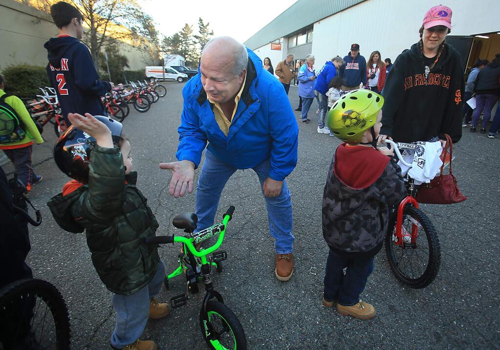 Innovative Screen Printing and Embroidery owner Mark Pippin gets a high five from Ayden Bishop, 4, as his brother Jeremiah Bishop, 6, waits with their mother Nichole McCarty after the two received free bikes from Pippin in Rohnert Park, Friday Dec. 16, 2016. (Kent Porter / The Press Democrat) 2016