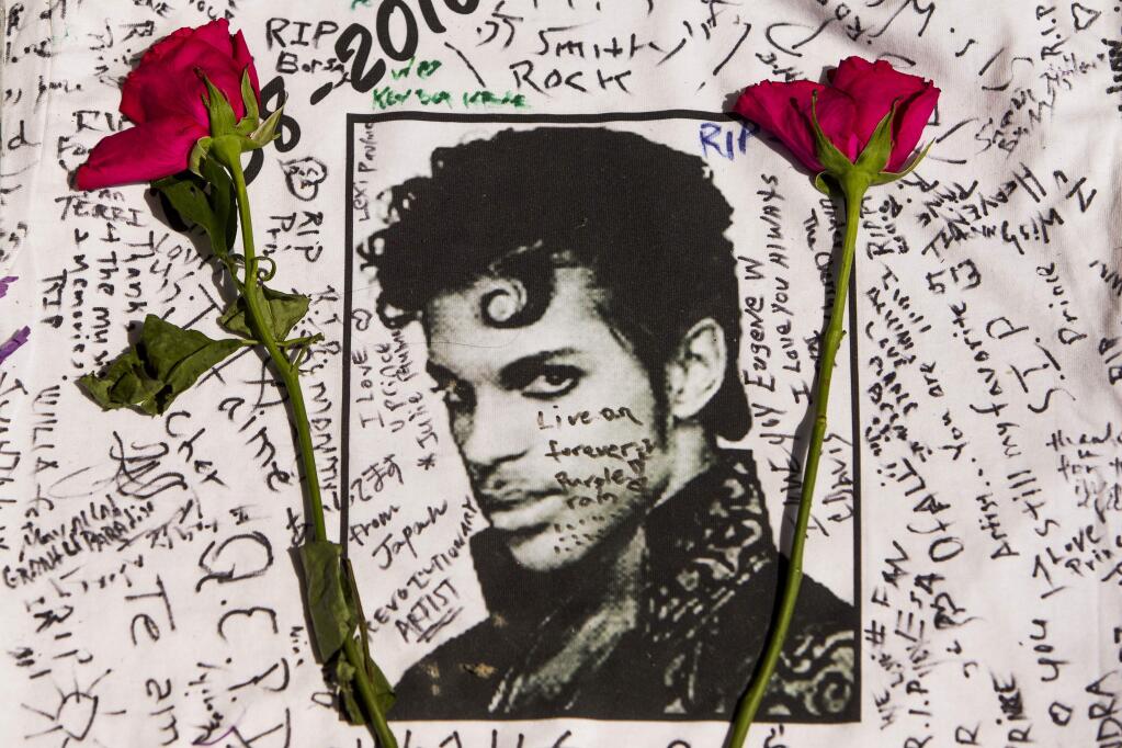 Flowers lay on a T-shirt signed by fans of singer Prince at a makeshift memorial place created outside Apollo Theatre in New York, Friday, April 22, 2016. The pop star died Thursday at the age of 57. (AP Photo/Andres Kudacki)