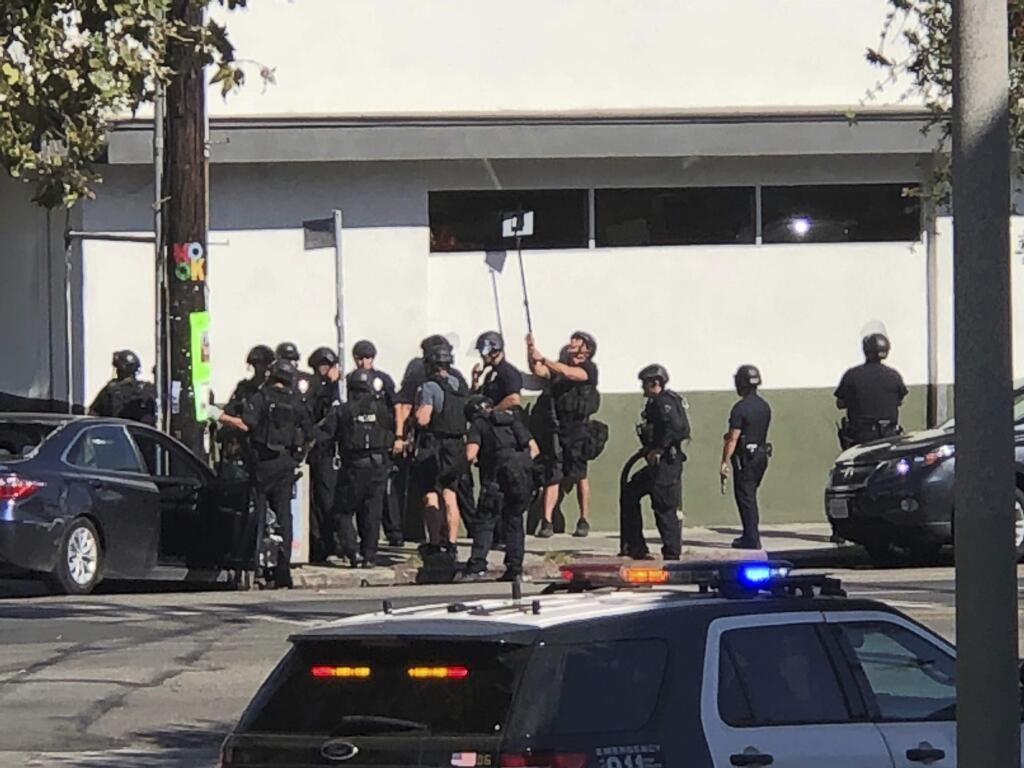 In this photo provided by Christian Dunlop, police officers use a mirror to see inside a Trader Joe's store in the Silver Lake neighborhood of Los Angeles on Saturday, July 21, 2018. Police believe a man involved in the standoff with officers shot his grandmother and girlfriend before firing at officers during a pursuit, then crashing outside the supermarket and running inside the store. (Christian Dunlop via AP)