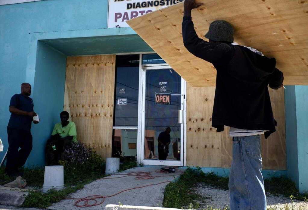 Workers board up a shop's window front as they make preparations for the arrival of Hurricane Dorian, in Freeport, Bahamas, Friday, Aug. 30, 2019. Forecasters said the hurricane is expected to keep on strengthening and become a Category 3 later in the day. (AP Photo/Ramon Espinosa)