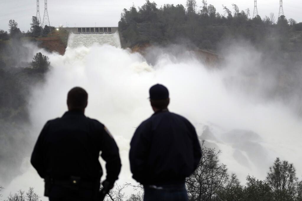 Two men watch as water gushes from the Oroville Dam's main spillway Wednesday, Feb. 15, 2017, in Oroville, Calif. The Oroville Reservoir is continuing to drain Wednesday as state water officials scrambled to reduce the lake's level ahead of impending storms. (AP Photo/Marcio Jose Sanchez)
