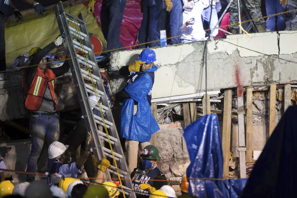 A ladder is raised to search and rescue team members during rescue efforts at the Enrique Rebsamen school in Mexico City, Mexico, Thursday, Sept. 21, 2017. A delicate effort to reach a young girl buried in the rubble of the school stretched into a new day on Thursday, a vigil broadcast across the nation as rescue workers struggled in rain and darkness to pick away unstable debris and reach her. Mexican navy officials now say the girl never existed. (AP Photo/Anthony Vazquez)
