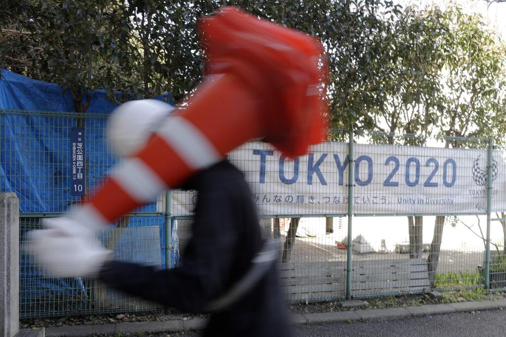 A worker on duty at a road construction site walks past a banner promoting the 2020 Olympic Games in Tokyo, Friday, March 20, 2020. The Olympic flame from Greece arrived in Japan even as the opening of the the Tokyo Games in four months is in doubt with more voices suggesting the games should to be postponed or canceled because of the worldwide virus pandemic. (AP Photo/Gregorio Borgia)