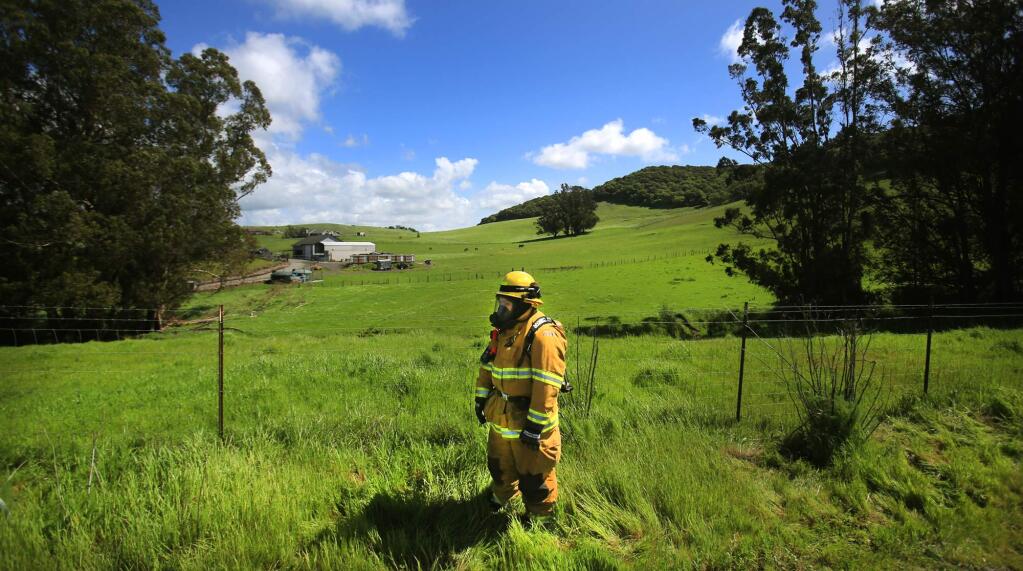 Wilmar Volunteer firefighter Bailey Maack stands at the ready as a Sonoma County Fire hazardous materials inspector investigates a substances in five gallon bucket that were left on the side of Chileno Valley Road near Petaluma, Wednesday March 22, 2017. (Kent Porter / The Press Democrat) 2017