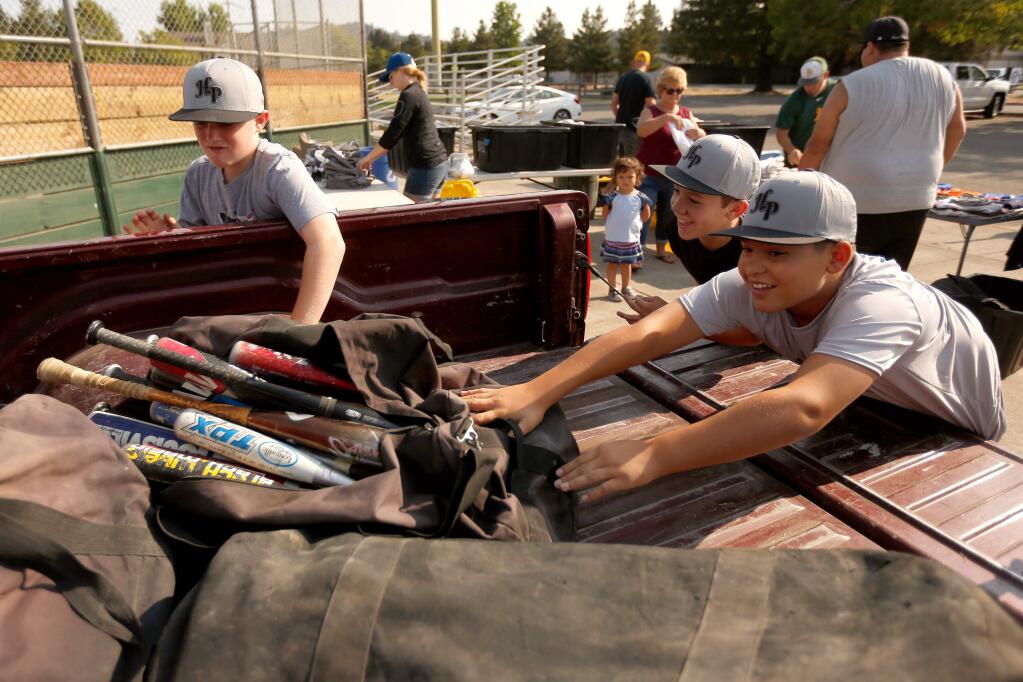 Mark West Little Leaguers TJ Karriker, left, Aidan Wedge and Dante Overholser load a heavy bag of baseball bats that will be delivered to victims of the Carr Fire, at the Mark West Youth Club Little League fields in Santa Rosa, California, on Saturday, August 11, 2018. Mark West Little League players and parents sort through donated items that will be delivered to victims of the Carr Fire in Redding. (Alvin Jornada / The Press Democrat)