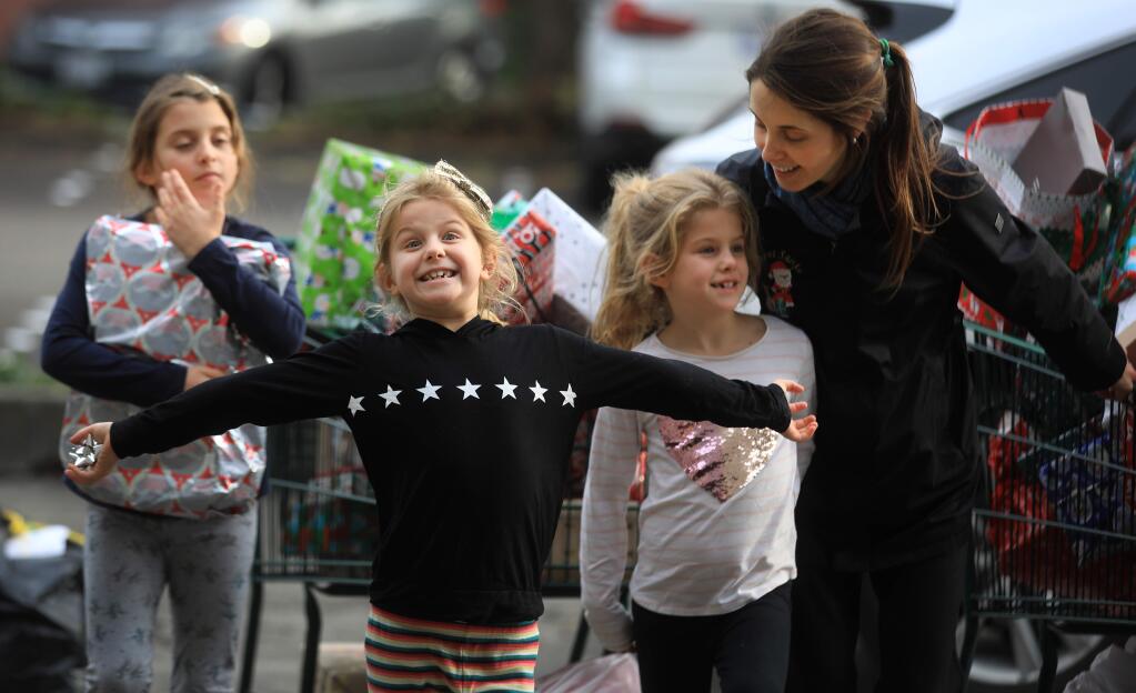 Secret Santa volunteers Riley Weiswasser, middle, announces the arrival of Christmas presents from her sisters Noa, left, and Haley, right, with their nanny Sophia Metzner, to the gift drop-off in downtown Santa Rosa, Friday, Dec. 20, 2019. (Kent Porter / The Press Democrat) 2019