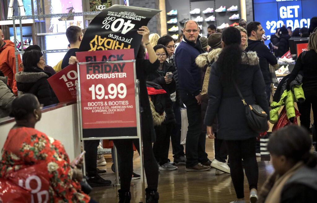 An employee posts discount signs for shoppers at Macy's department store during Black Friday shopping, Friday Nov. 29, 2019, in New York. Black Friday shoppers fought for parking spots and traveled cross-state to their favorite malls, kicking off a shortened shopping season that intensified the mad scramble between Thanksgiving and Christmas. (AP Photo/Bebeto Matthews)