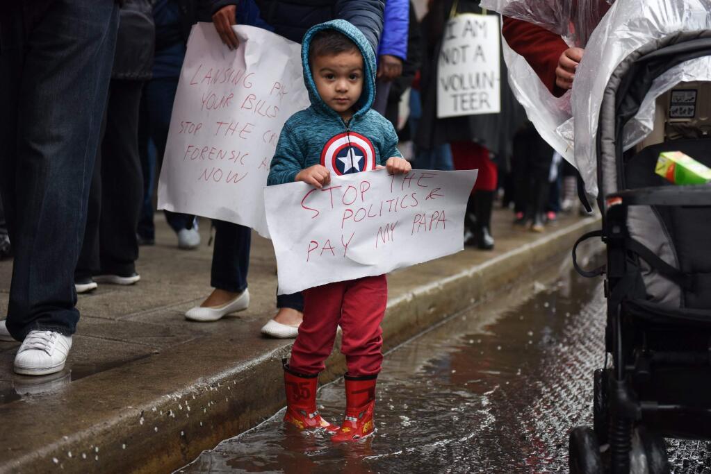 Kevin Casillas Jr., 4, walks through a puddle while holding a sign supporting his father who is a Detroit Public School teacher, Monday, May 2, 2016, in Detroit. Nearly all of Detroit's public schools were closed Monday and more than 45,000 students missed classes after about half the district's teachers called out sick to protest the possibility that some of them will not get paid over the summer if the struggling district runs out of cash. (Tanya Moutzalias/The Ann Arbor News-MLive Detroit via AP)