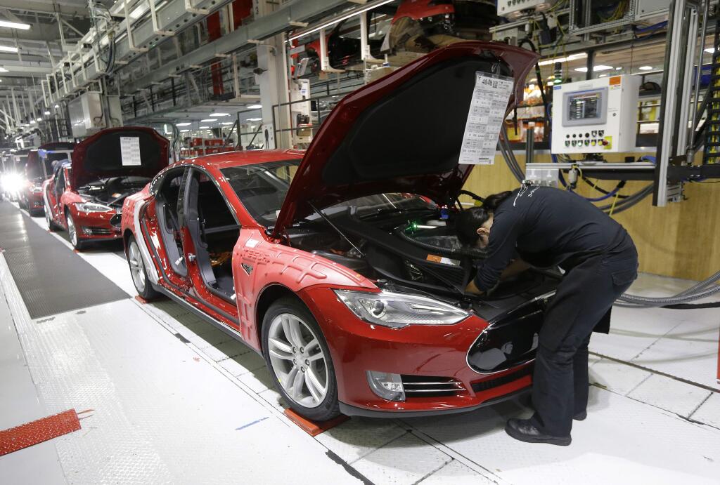 FILE - In this May 14, 2015, file photo, Tesla employees work on a Model S cars in the Tesla factory in Fremont, Calif. The parking lot was full at Tesla's California electric car factory Monday, May 11, 2020, an indication that the company was resuming production in defiance of an order from county health authorities. (AP Photo/Jeff Chiu, File)