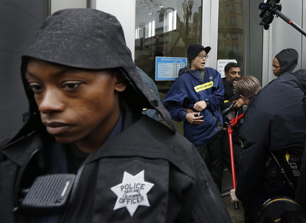An Oakland police officer stands guard at the front door of police headquarters as another uses bolt cutters to free protestors who chained themselves to it Monday, Dec. 15, 2014, in Oakland, Calif. Demonstrators blocked streets around Oakland police headquarters and chained themselves to the front of the building Monday to protest recent grand jury decisions not to indict white officers who killed unarmed black men in Ferguson, Missouri, and New York. (AP Photo/Ben Margot)