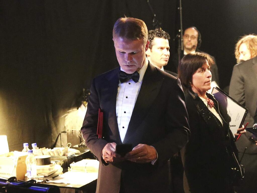 FILE - In this Feb. 26, 2017, file photo, PwC accountant Brian Cullinan, center, holds red envelopes under his arm while using his cell phone backstage at the Oscars at the Dolby Theatre in Los Angeles. PwC accountants won't be allowed to have their cellphones backstage during future Oscar telecasts. Film academy president Cheryl Boone Isaacs sent an email to academy members Wednesday, March 29, 2017, detailing the new protocols established for announcing Oscar winners after the best-picture flub at last month's Academy Awards. Boone Isaacs blamed Cullinan's distraction for the error. (Photo by Matt Sayles/Invision/AP, File)