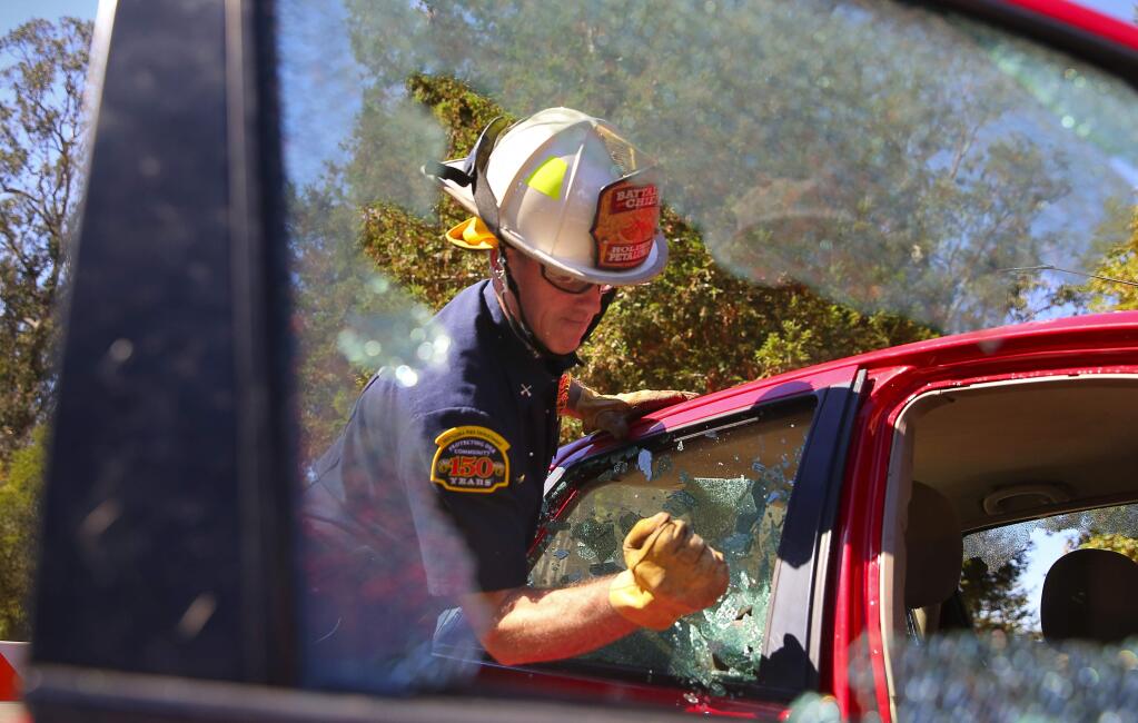 Petaluma Fire Department Battalion Chief Jeff Holden uses a handlheld tool to break a side window, during a submerged vehicle demonstration at Lake Ralphine, in Santa Rosa, on Monday, September 26, 2016. (Christopher Chung/ The Press Democrat)