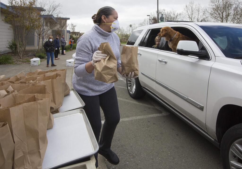 Irma Alvarado Pizano hands breakfast and lunch bags to a student's parents at the drive-through at Adele Harrison Middle School on Monday, Mar. 23. (Photo by Robbi Pengelly/Index-Tribune)
