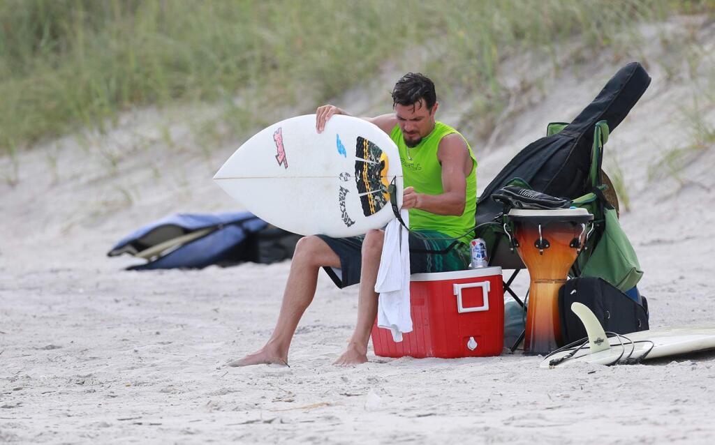 Zachary Zepeda, 36, of Richlands, N.C., waxes his board before heading into the surf in Surf City, N.C., Tuesday, Aug. 30, 2016. Crowds thinned Tuesday on the beaches of North Carolina's Outer Banks ahead of a tropical weather system that threatened to bring strong winds and heavy rains that could flood low-lying areas. (John Althosue/The Daily News via AP)
