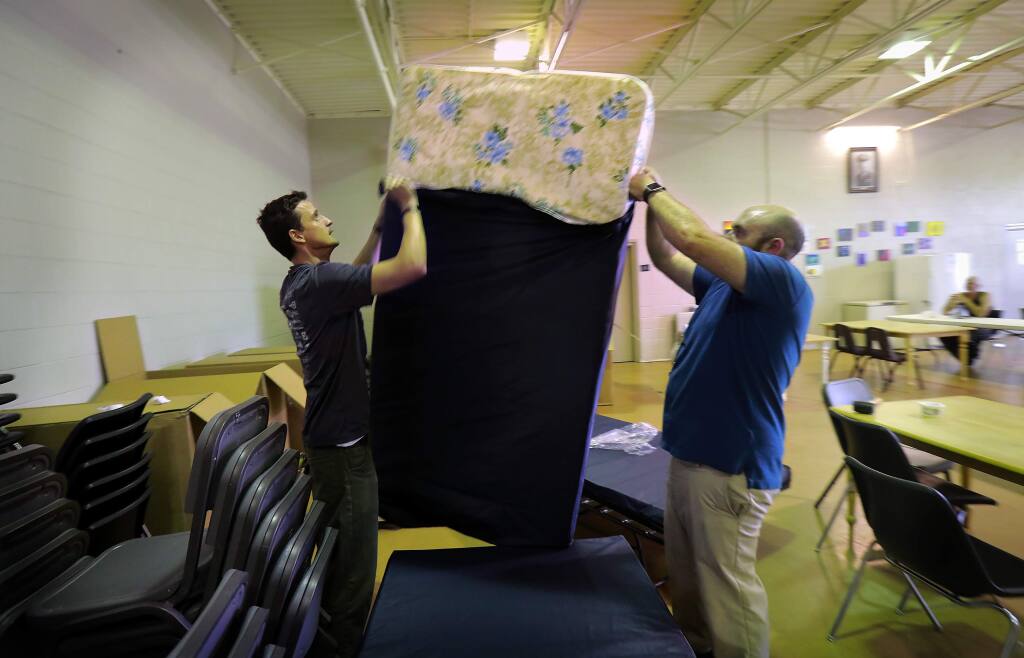 Catholic Charities employees Brendan Ward, left, and Burleigh Termo unload put a cover on one of 50 new beds at the Sam L. Jones Hall homeless shelter in Santa Rosa on Friday. (photo by John Burgess/The Press Democrat)