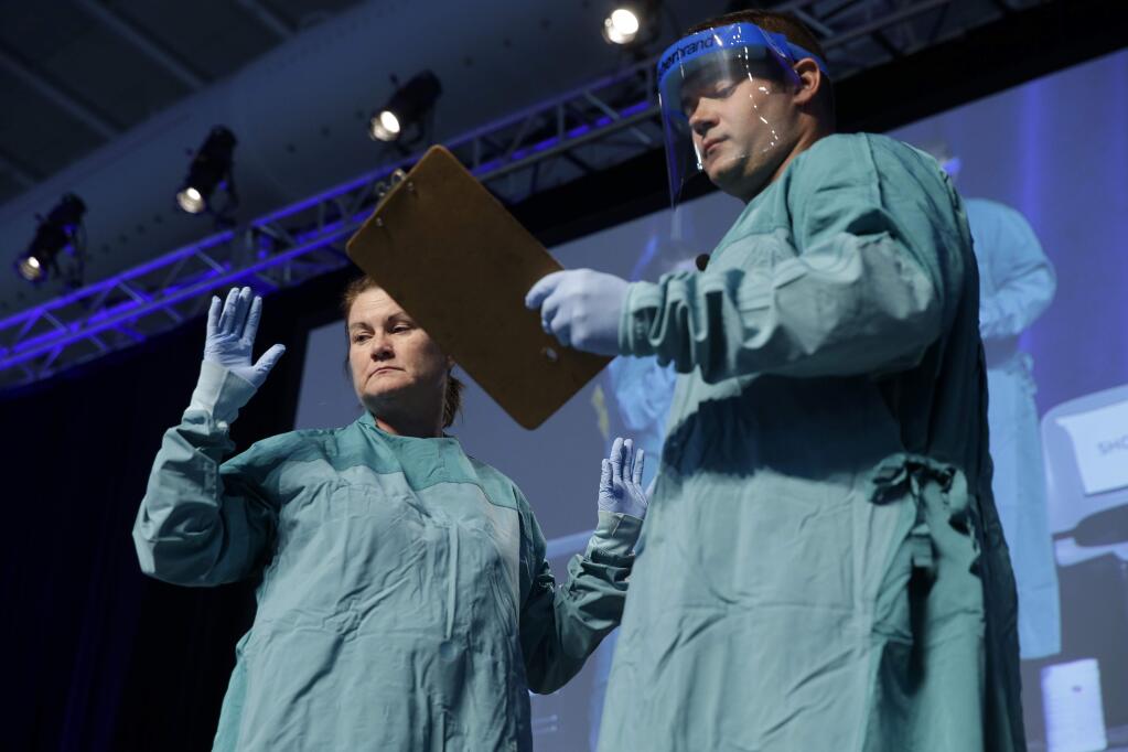 FILE- In this Oct. 21, 2014, file photo, Nurse Barbara Smith, left, and Dr. Bryan Christensen demonstrate the proper way for health care workers to use personal protective equipment when dealing with Ebola during an education session in New York. (AP Photo/Seth Wenig, File)