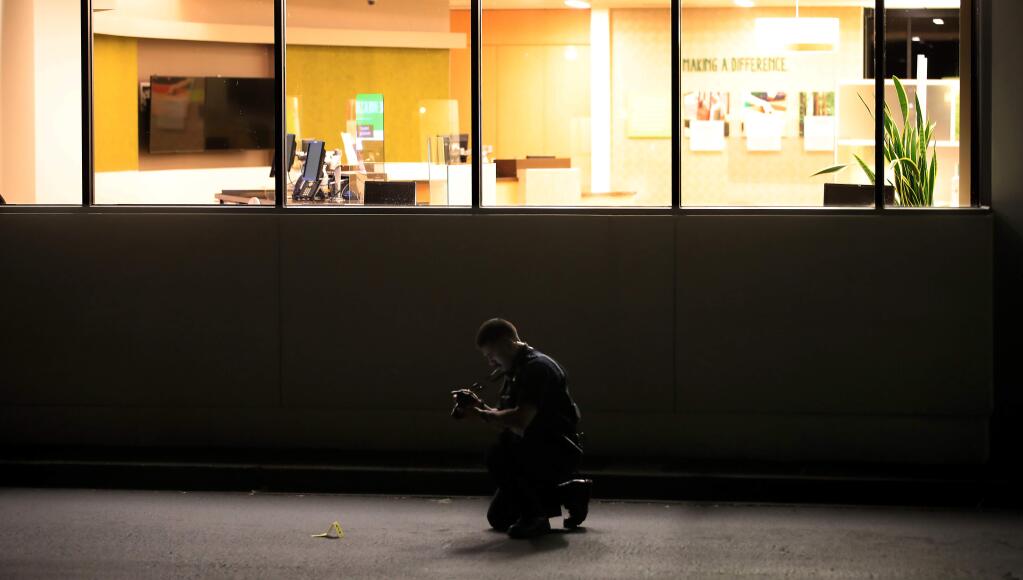 A Rohnert Park Department of Public Safety officer photographs the trail of evidence markers at scene of a shooting in the drive-up ATM area that resulted in one person dead, after the victim was found in the westbound lane of Rohnert Park Expressway near State Farm Drive on Wednesday, May 27, 2020. (Kent Porter/The Press Democrat)