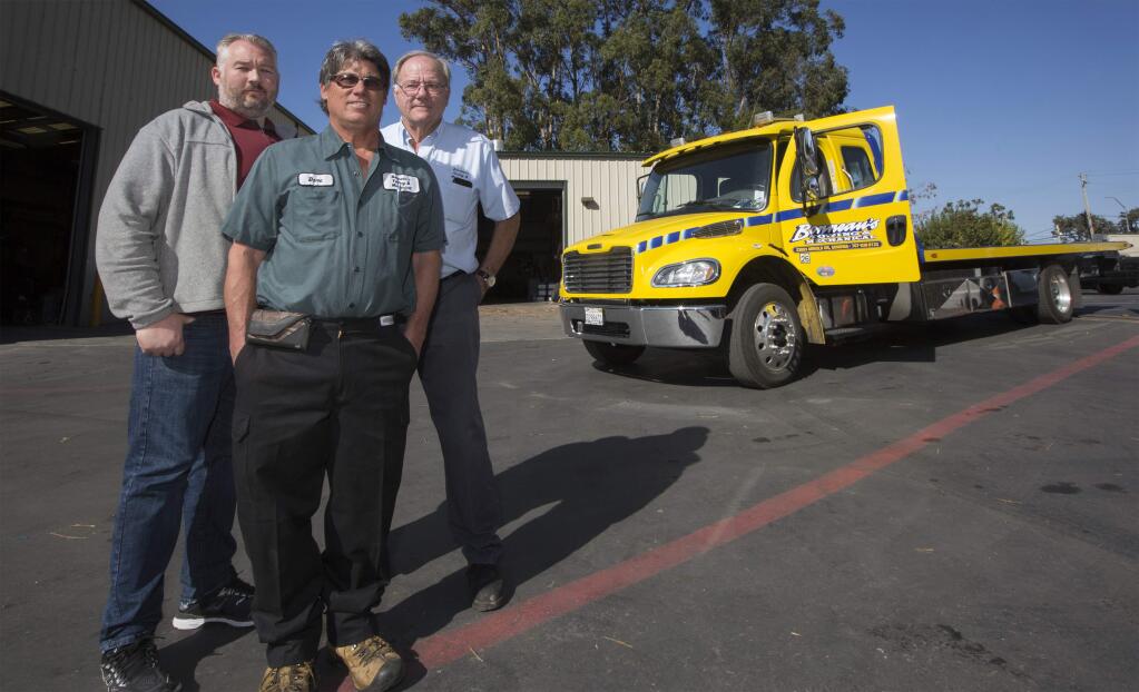From left, Chris Banbury, Dave Hulbert, and Dan Banbury, with one of their familiar tow trucks at the location of their vehicle maintenance garage, gas station and deli on Arnold Dr. and Highway 121. (Photo by RobbiPengelly/Index-Tribune)