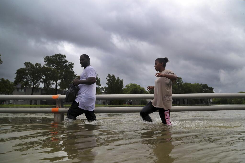 Residents walk through high waters, the remnants of Hurricane Harvey, on Watonga Boulevard, Sunday, Aug. 27, 2017, in Houston. The remnants of Hurricane Harvey sent devastating floods pouring into Houston Sunday as rising water chased thousands of people to rooftops or higher ground. (Marie D. De Jesus/Houston Chronicle via AP)