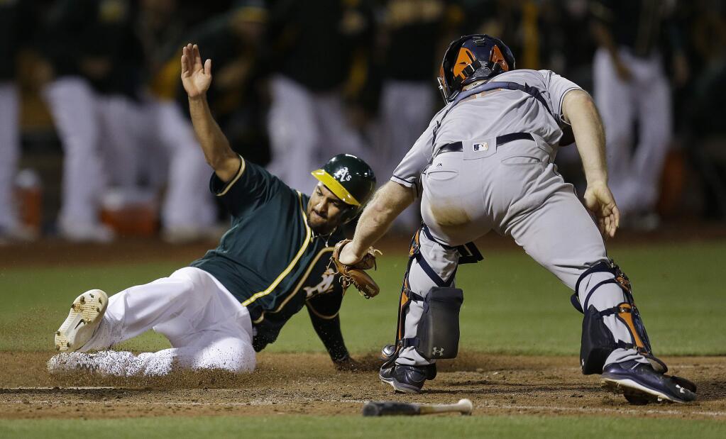 Oakland Athletics' Marcus Semien, left, slides to score past Houston Astros catcher Evan Gattis in the tenth inning of a baseball game Tuesday, July 19, 2016, in Oakland, Calif. Semien scored on a hit by Josh Reddick. (AP Photo/Ben Margot)