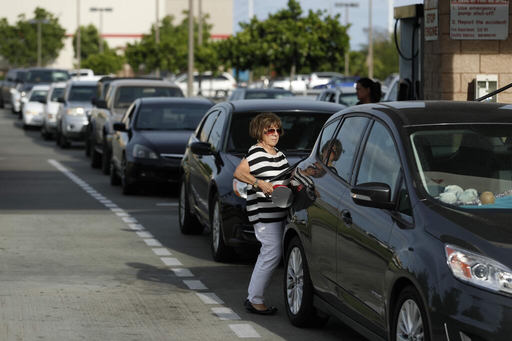 A woman fills up her car as other vehicles line up behind her for gasoline at a Costco in preparation for Hurricane Lane, Wednesday, Aug. 22, 2018, in Kapolei, Hawaii. (AP Photo/John Locher)
