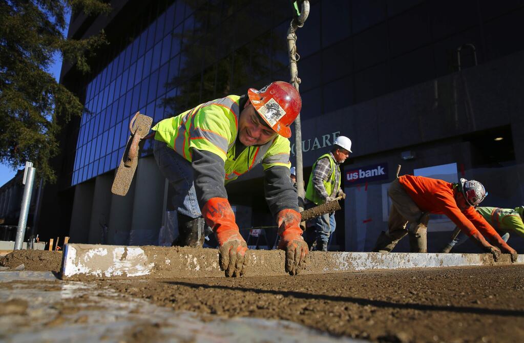 Michael Ortiz , left, works with other construction workers to level wet cement Santa Rosa's Old Courthouse Square on Friday, December 30, 2016. (Christopher Chung/ The Press Democrat)