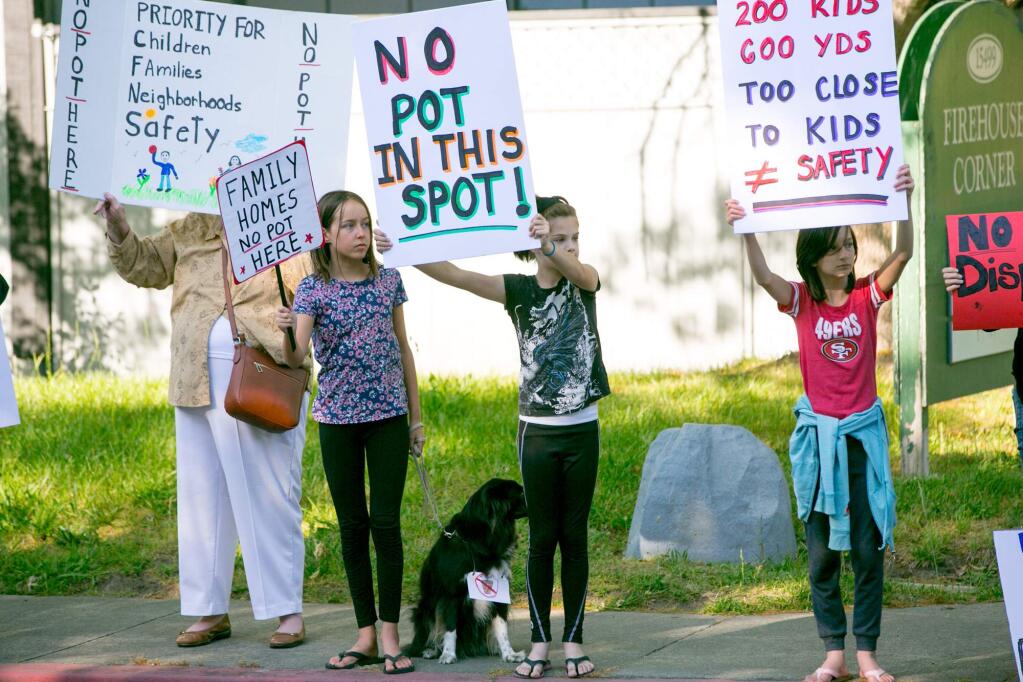 Local activists Riina Palmgren, Shalie the dog, Abbie Lair, at center, and Francesca Fidani wave protest signs in May of 2018 at the site of a proposed cannabis dispensary at Arnold Drive and Madrone Road, Glen Ellen. (Photo by Julie Vader/Special to the Index-Tribune)