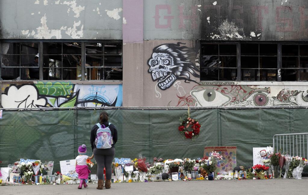 FILE - This Dec. 13, 2016 file photo shows flowers, pictures, signs and candles, are placed at the scene of a warehouse fire in Oakland, Calif. A former tenant of an Oakland warehouse says police were called to the unlicensed residence several times to help with evictions, and even knew the leaseholder by name. Jose Avalos, a woodworker who moved into the Ghost Ship two years before a deadly fire killed 36 partygoers a year ago, testified Thursday, Dec. 7, 2017, on the second day of a preliminary hearing in Alameda County Superior Court for two men charged with involuntary manslaughter in their deaths. (AP Photo/Marcio Jose Sanchez, File)