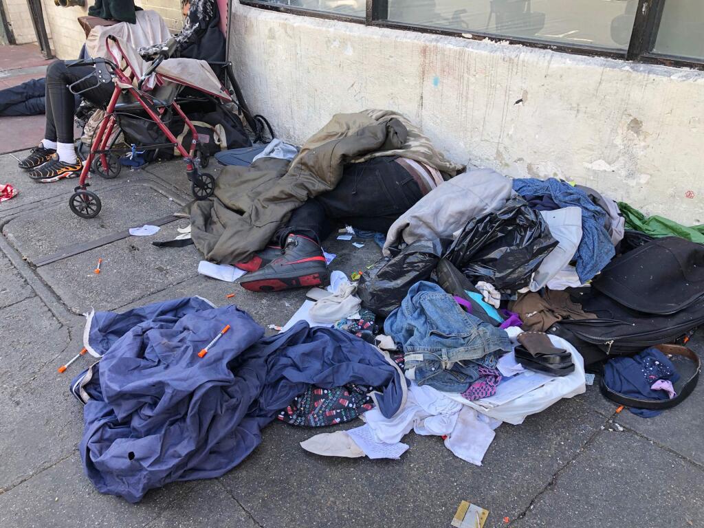 FILE - In this July 25, 2019, file photo, sleeping people, discarded clothes and used needles are seen on a street in the Tenderloin neighborhood in San Francisco. A center for people experiencing methamphetamine-induced psychosis will open in San Francisco as the city struggles with a rise in drug overdoses and rampant street drug use. The San Francisco Chronicle reports the center will open in late spring. (AP Photo/Janie Har, File)