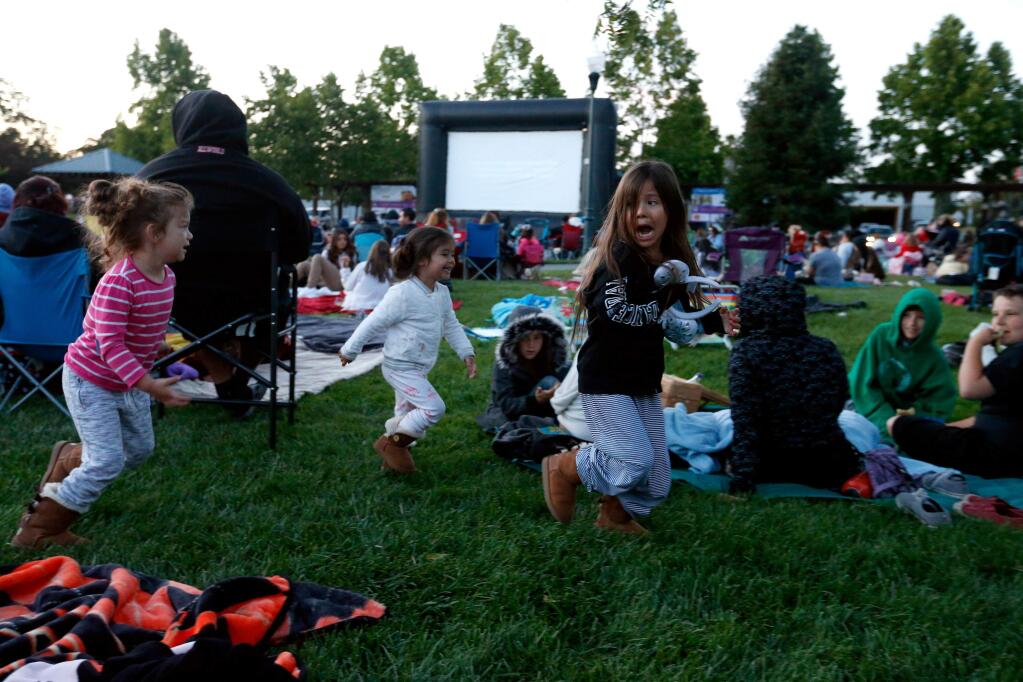 Briella Solano, 5, center right, playfully runs away from her sister Mia Solano, 3, and friend Jocelyn Marlow, 4, while they wait for the movie to begin at the Tuesday Night Kids' Movie at the Windsor Town Green in Windsor, California on Tuesday, June 14, 2016. (Alvin Jornada / The Press Democrat)