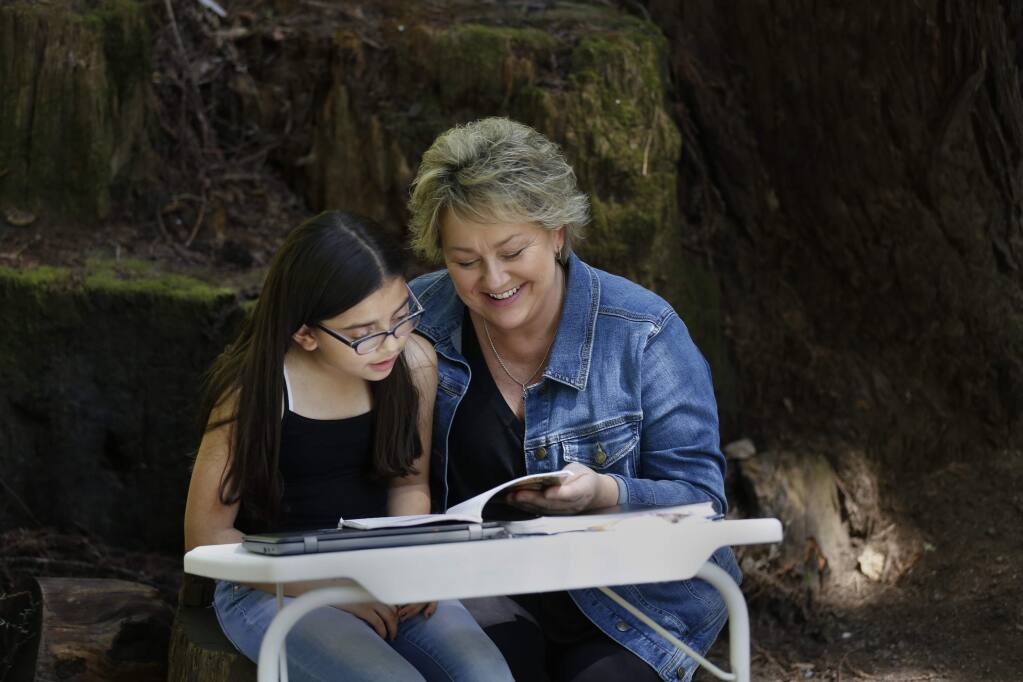 Cynthia Ferrera, a parent liaison at Lilliput Children's Services and her granddaughter, Tatianna Rodriguez, 8, read together in an outdoor classroom set up outside their home in Rio Nido on Thursday, April 23, 2020. (BETH SCHLANKER/ The Press Democrat)