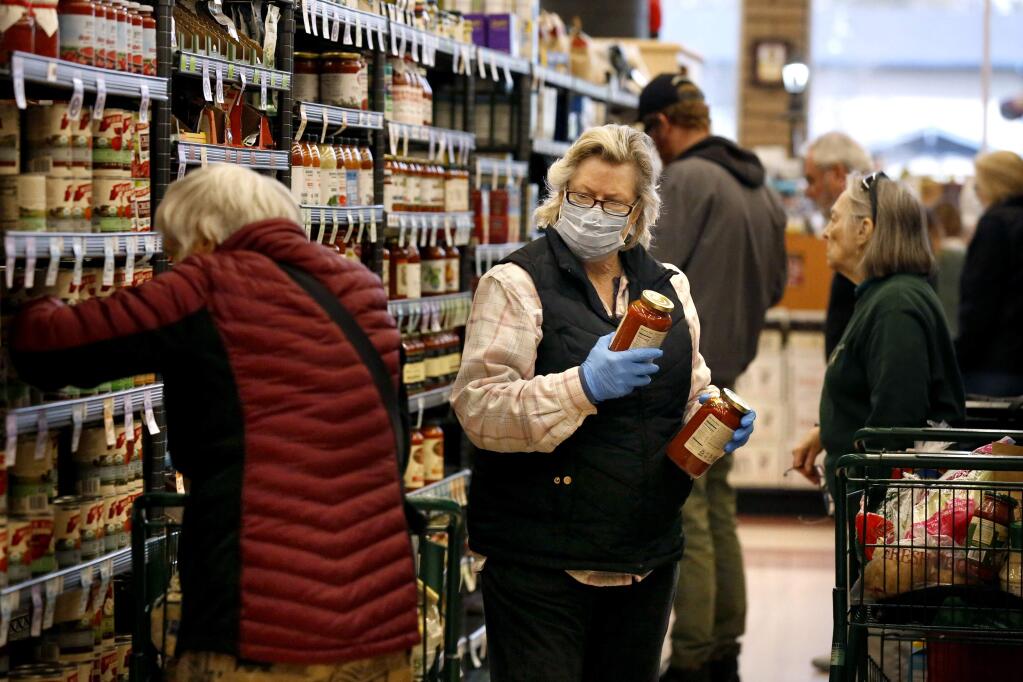 Belinda, who wished not to give her last name, takes precautions with a mask and gloves as she shops in the canned good aisle at Oliver's Market in the Montecito Center in Santa Rosa on Tuesday, March 17, 2020. (Beth Schlanker / The Press Democrat)