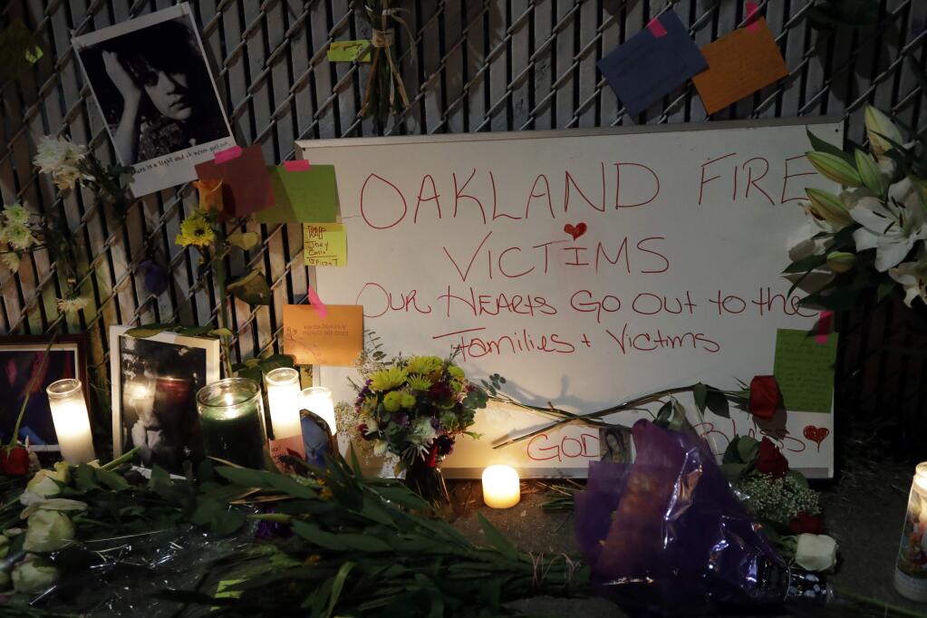 FILE - In this Monday, Dec. 5, 2016, file photo, candles, photos and flowers are placed at a makeshift memorial near the site of a massive warehouse fire in Oakland, Calif. Micah Allison, the wife of the founder of a ramshackle Oakland artists' colony where dozens of people burned to death in a fire last month says she's sorry about what happened but is angry about what she called 'pretty terrible' treatment by the media and ex-neighbors. (AP Photo/Marcio Jose Sanchez, File)